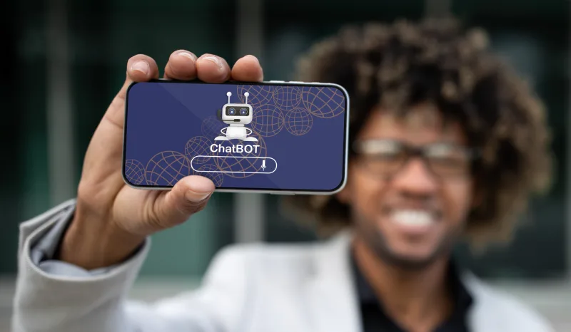 A person holding a smartphone displaying a ChatBOT logo against a blurred background, emphasizing technology and communication.
